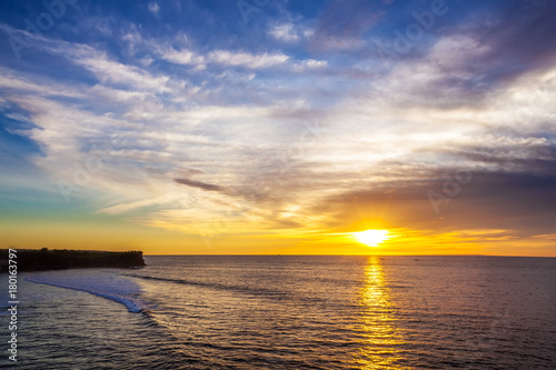 Silhouette of a cliff against the background of an orange sunset. Sea waves break on the rocks. Sunset on Jimbaran  South Kuta  Bali  Indonesia.