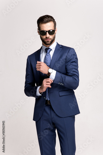 Getting ready for a date. Handsome young man in sunglasses adjusting his sleeve while standing against white background.