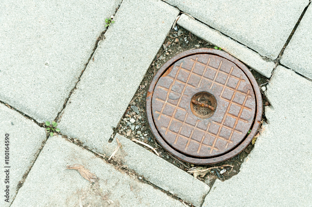 Rusty manhole cover of access point for a shut off valve to a water main along a sidewalk