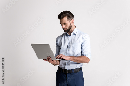 Having some emails to look through. Handsome young man using his laptop while standing against white background.
