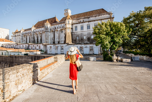 Woman in red dress walking back on the old university building background in Coimbra city in the central Portugal