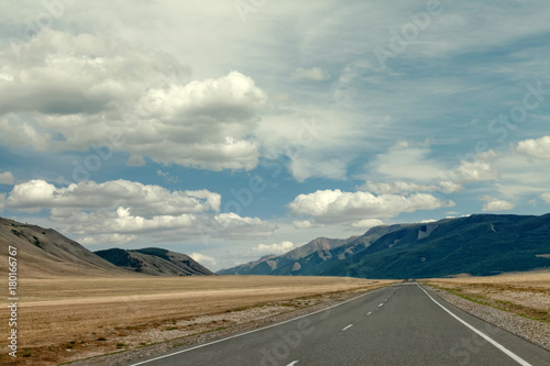 highway between mountains and a blue sky with large clouds