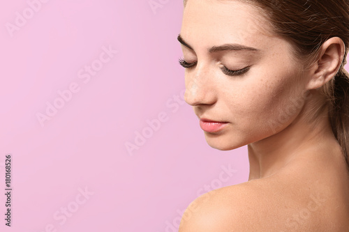 Young woman with eyelash extensions on color background