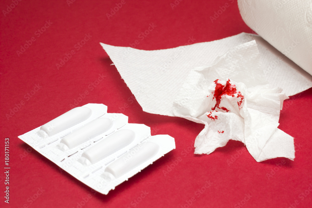 A photo of rectal candles, used shits of bloody toilet paper and a toilet paper roll. Blood