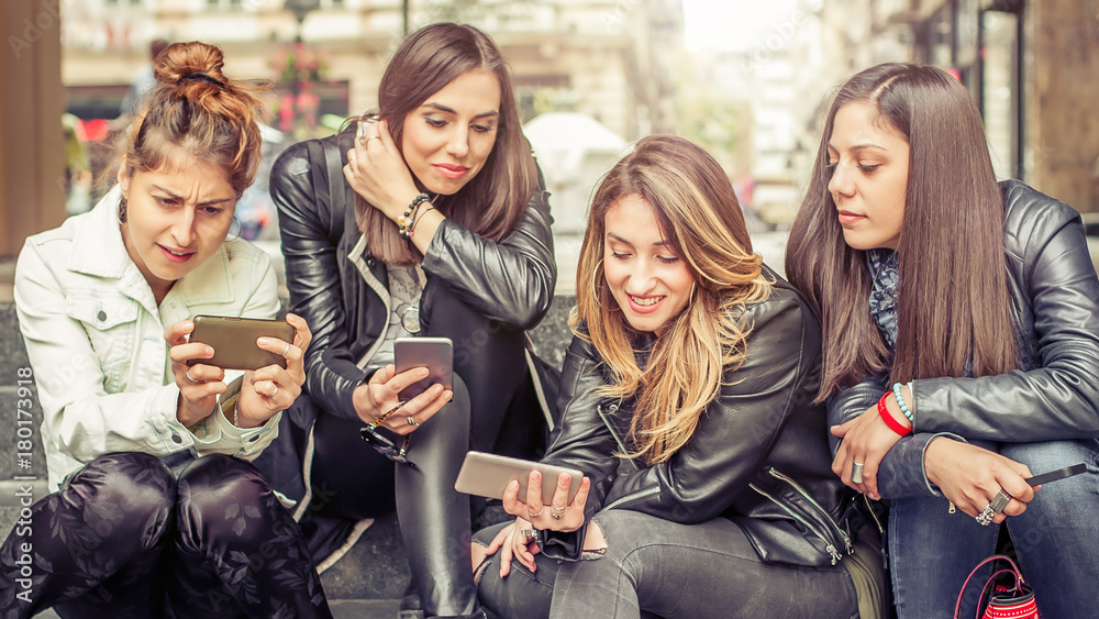 Happy girl friends sitting on the city stairs with smartphone Happy girl friends sitting on the city stairs with smartphone