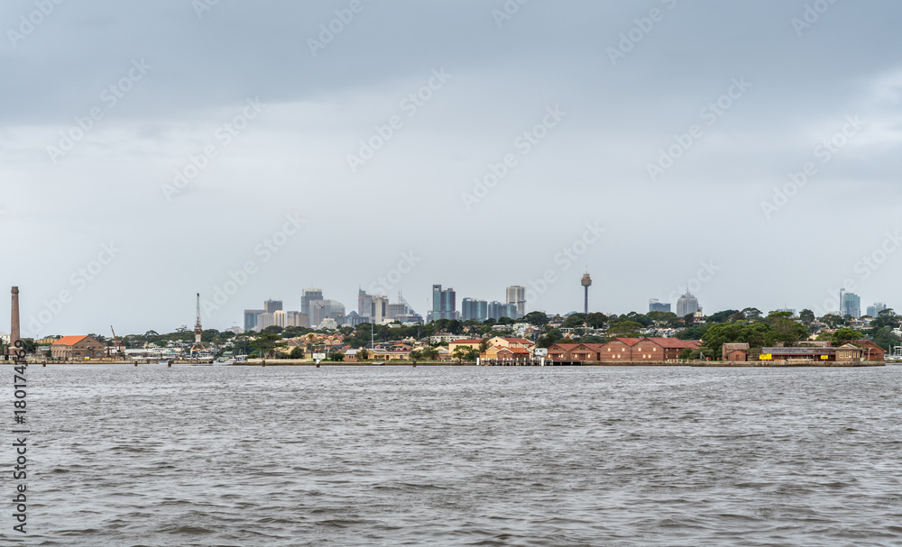 Parramatta, Australia - March 24, 2017: Looking towards skyline of downtown Sydney standing on boat off Drummoyne Wharf point. Lower built housing and warehouses on closest shore. Parramatta, Australia - March 24, 2017: Looking towards skyline of downtown Sydney standing on boat off Drummoyne Wharf point. Lower built housing and warehouses on closest shore.
