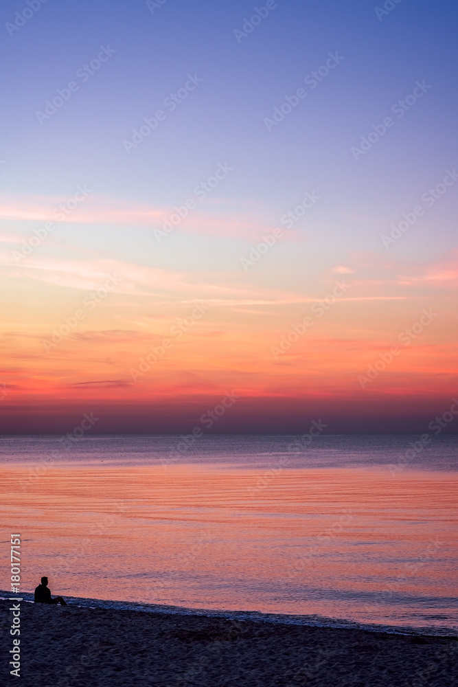 Lonely man sitting on the sea beach at sunset