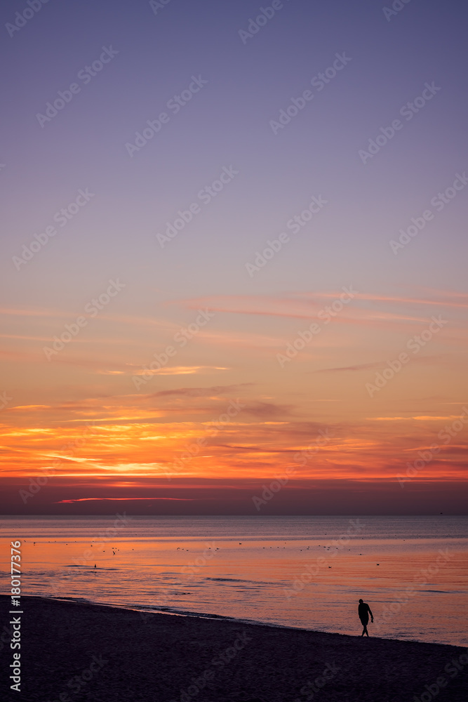 Lonely man walking on the sea beach at sunset