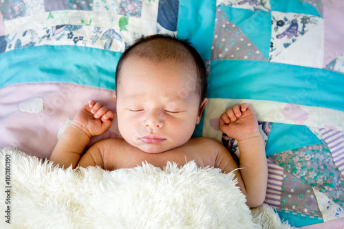 New Baby Boy sleeping wrapped in fluffy cream blanket on pathwork quilt photo