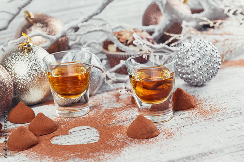 Whiskey or liqueur, truffle chocolate candies in cocoa powder and christmas decorations on white wooden background.