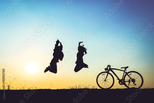 silhouette of young woman and boy jumping on sunset sky with bicycle on the prairie at yellow evening horizon sea yellow sunset heaven background Outdoor.