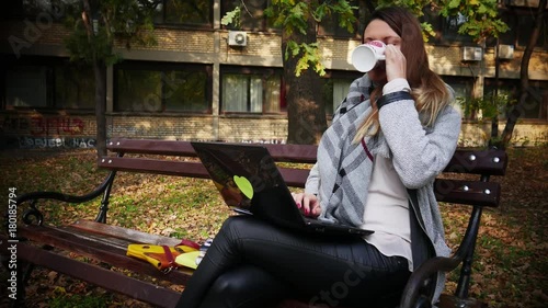 2in1, a young woman in outdoor office working on a laptop and drinks coffee / tea from a cup of red hearts, park in autumn photo