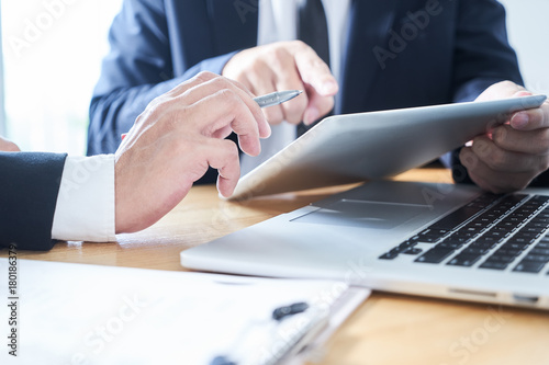 Two businessman using laptop and digital tablet to discuss finance and marketing solution .