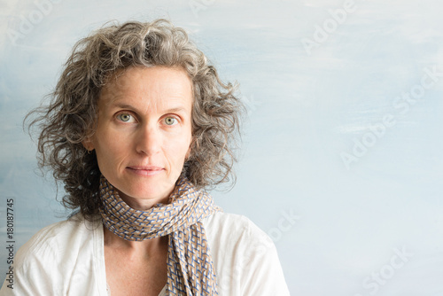 Portrait of middle aged woman with wavy grey hair and scarf against blue background (selective focus)