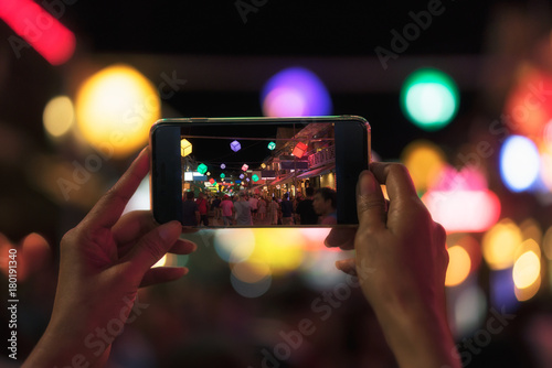 Young Asian traveler taking photo with mobile phone in pub and street road at night in Cambodia
