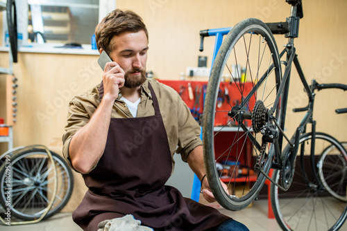 Bike repairman speaking on smartphone during work in repair service