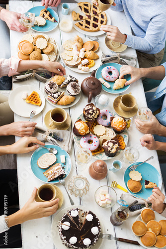 Group of friends gathered by birthday table having tea with variety of sweet homemade pastry