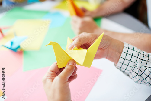 Foto Human hands folding sheet of yellow paper while making origami bird