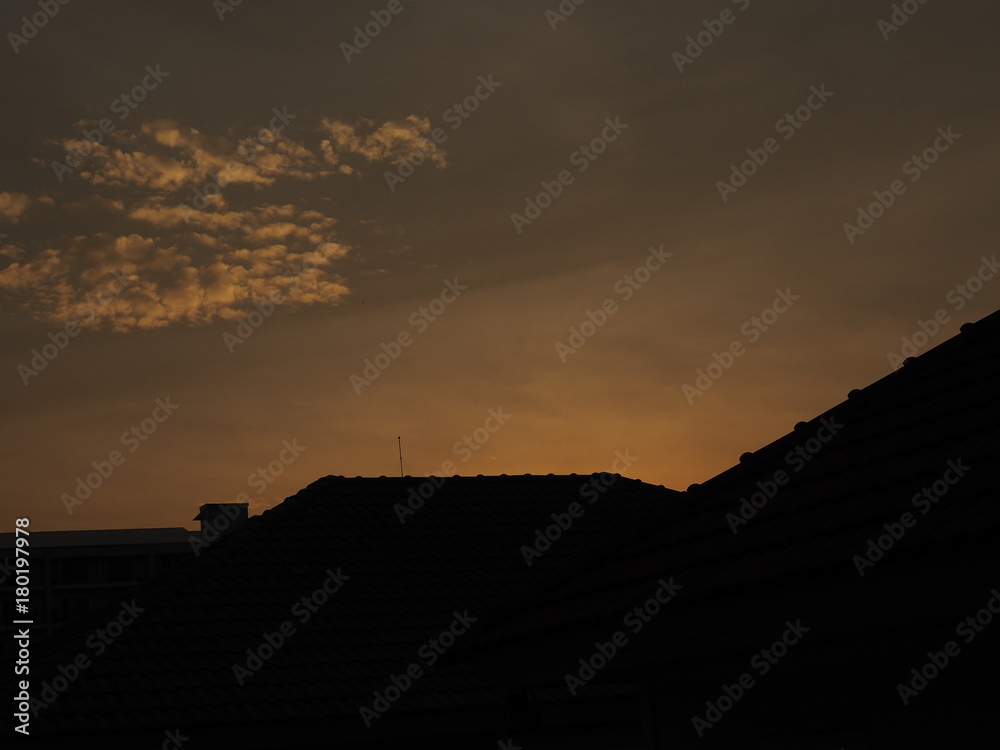Sunset dark black and yellow orange clear sky with silhouette shadow of village house roof, and small clouds background