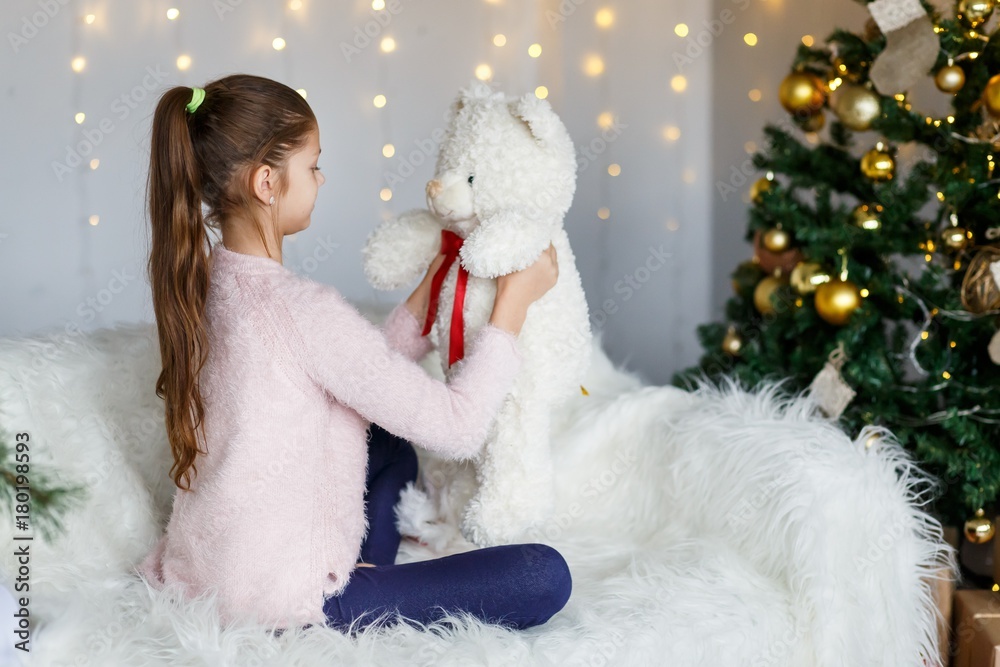 A brunette gilr in front of fur-tree and fireplace with candles and gifts. A surprised girl. A girl dreaming. New year's eve. Christmas eve. Cozy holiday at the fur-tree with lights and gold decor.