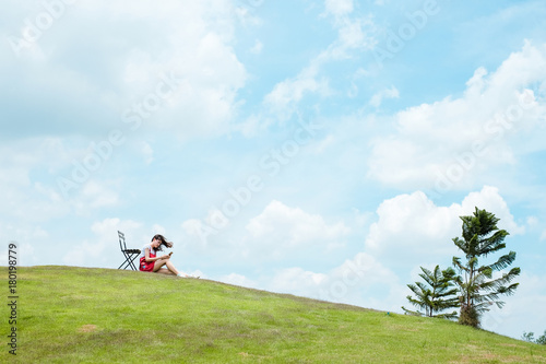 Young woman wearing red dress smiling enjoy and small wooden chair on little mountain with blue sky background with copy space.lonely concept.