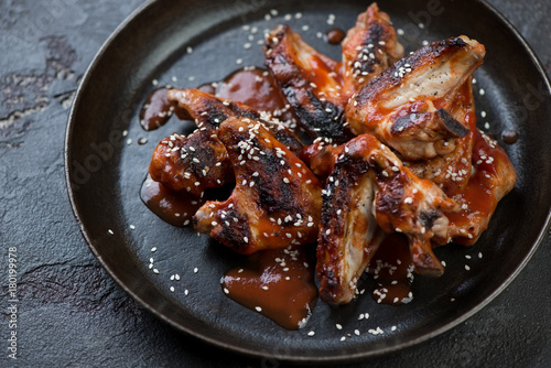 Barbecued chicken wings served with sauce and sesame seeds in a metal plate, studio shot