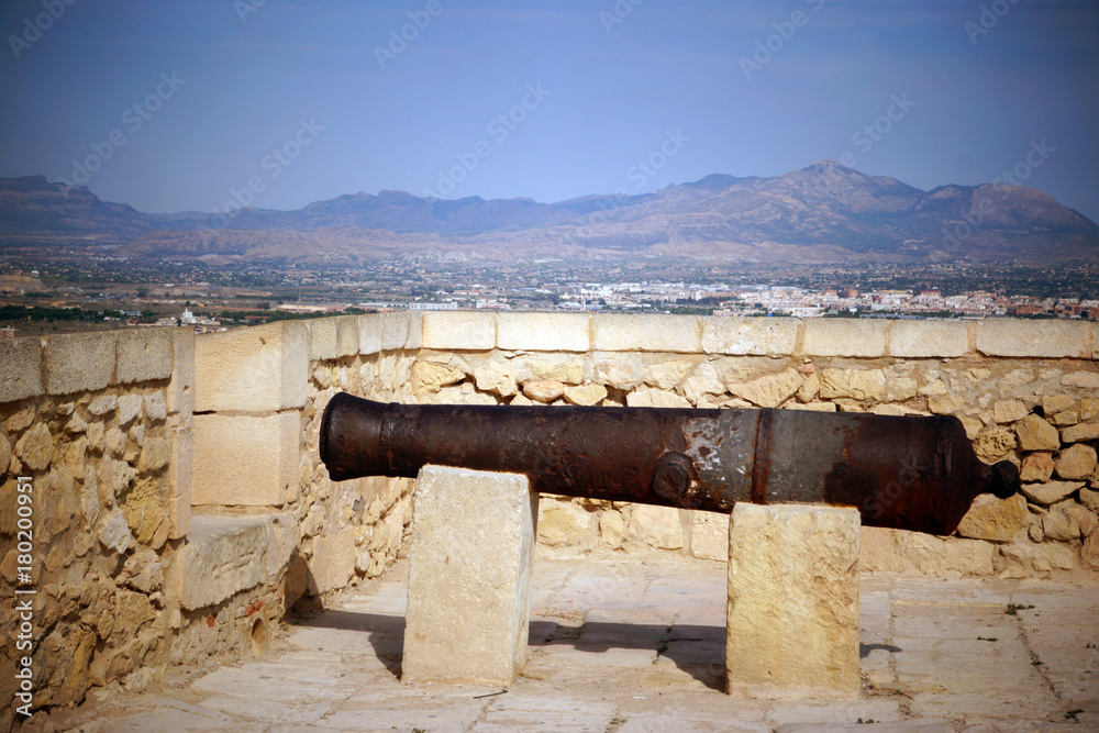 An old cannon stands on top of an ancient castle on a mountain