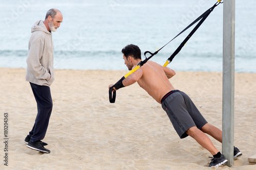 Athletic man making suspension training exercise on the beach with coach © Adam Gregor