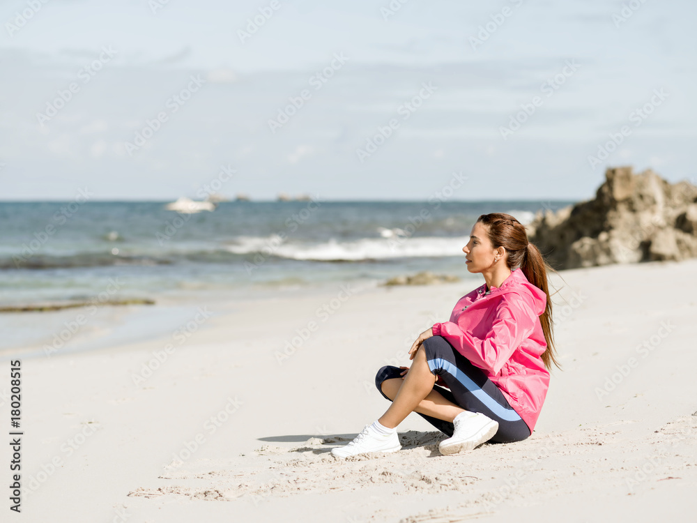 Young woman sitting at the beach in sportswear Young woman sitting at the beach in sportswear