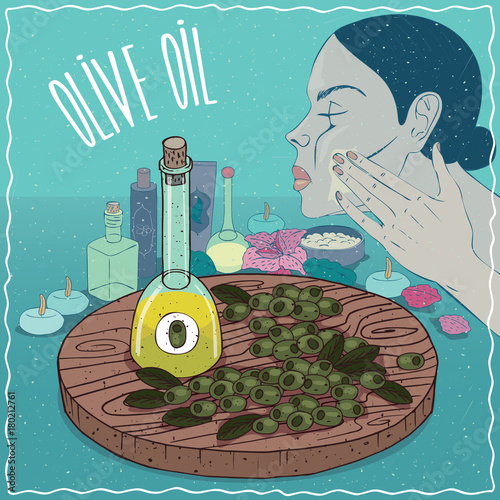 Glass Decanter of Olive oil and fruits of Olea europaea plant. Girl applying facial mask on face. Natural vegetable oil used for skin care