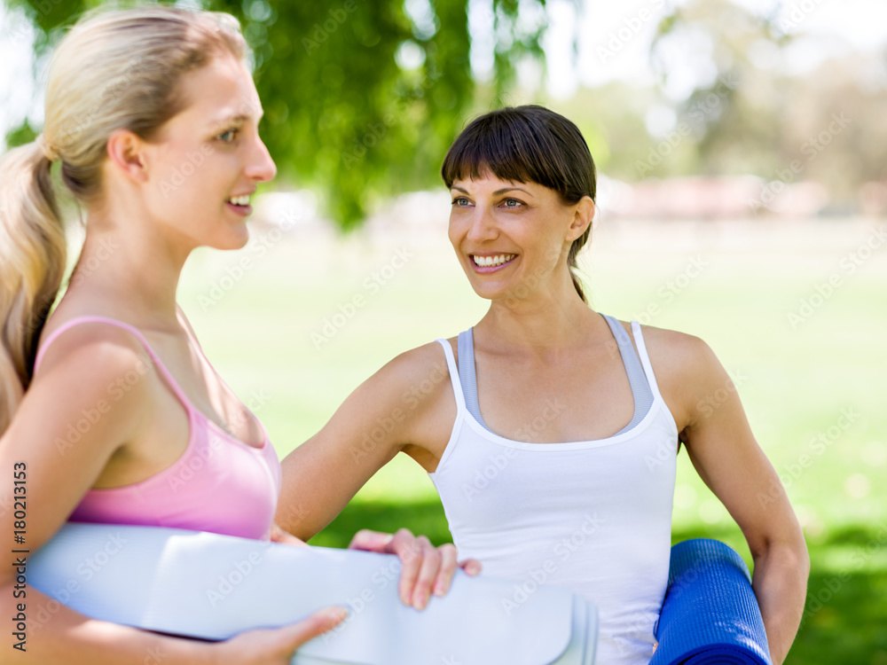 Fototapeta premium Two young women with a gym mat chatting in the park