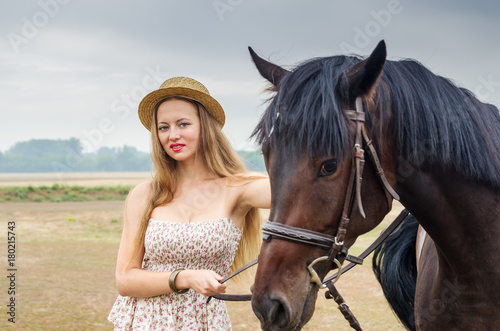 Girl in a straw hat and summer dress, posing with a horse / Photographed in Russia, at the racetrack in Orenburg
