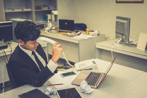 Businessman stress from hard work on the desk at office dark tone.take with boss on telephone
