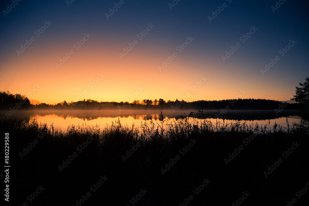 Fototapeta premium A beautiful sunrise on a lake with a raising mist. Beautiful morning in wetlands in Latvia. Autumn landscape in bright colors.