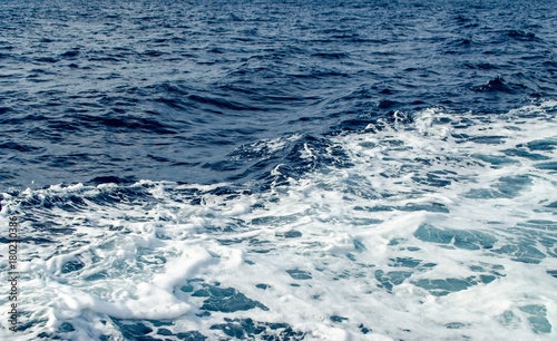 A Blue Trail Waves Surface Foam of Cruise Line After Speed Boat Passing in Ocean with Beautiful Blue Sky Background.