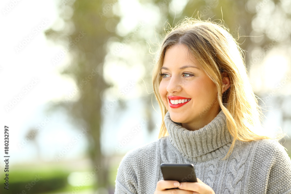 Happy girl looking away and holding phone in winter Happy girl looking away and holding phone in winter