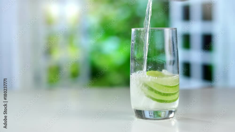 A refreshing drink being poured into a glass with ice, lemon and lime