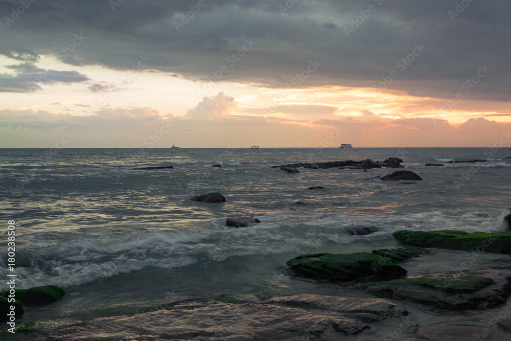 Sunset in Cambodia at the seaside. Sea waves roll on sands and rocks.