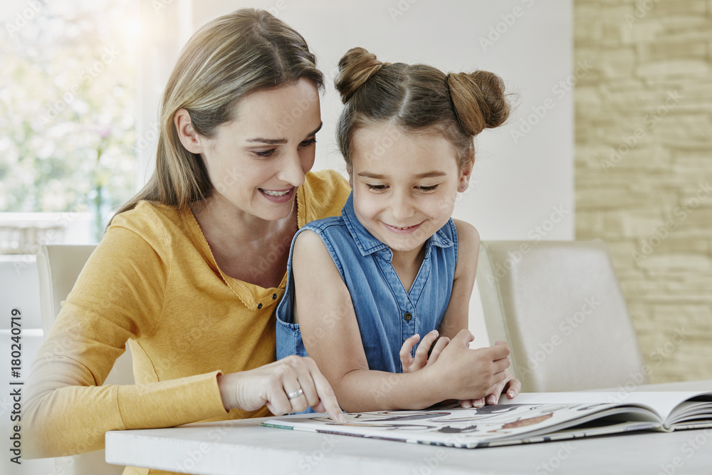 Happy mother with daughter at home looking at picture book Happy mother with daughter at home looking at picture book