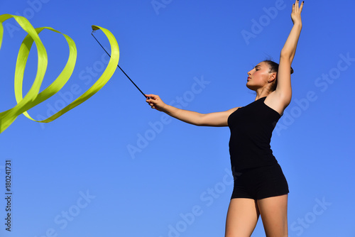 Woman gymnast swirl green ribbon on blue sky background © Volodymyr