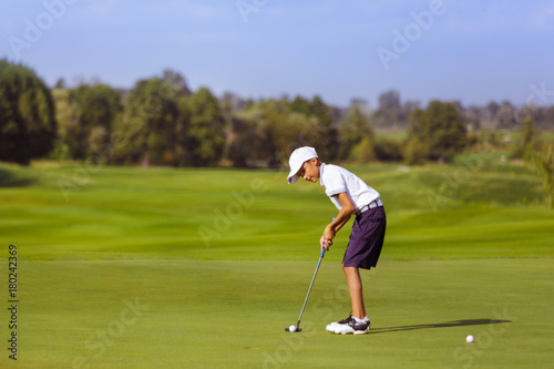 Boy golf player putting at green at sunny day