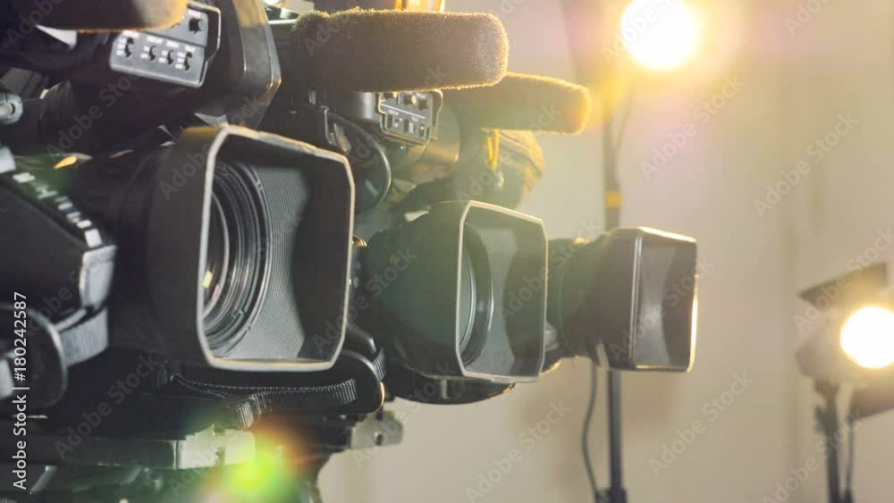 Three video cameras brightly lit by spotlights. 