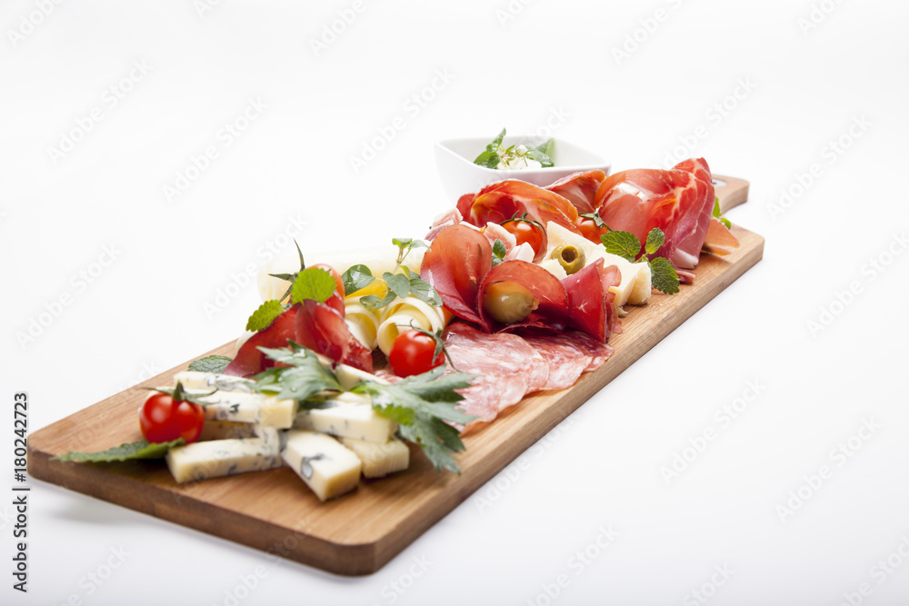 Antipasto platter cold meat plate with grissini bread sticks, prosciutto, slices ham, beef jerky, meats, sausages, salami, ham, olives, laid and arugula on cutting board on wooden background. Antipasto platter cold meat plate with grissini bread sticks, prosciutto, slices ham, beef jerky, meats, sausages, salami, ham, olives, laid and arugula on cutting board on wooden background.