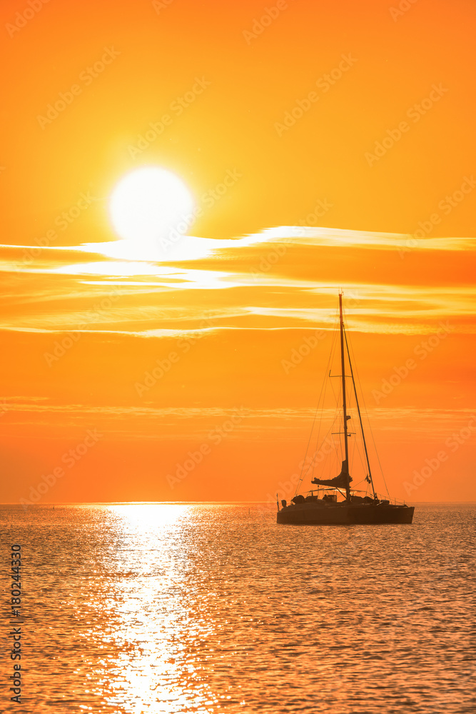 Catamaran glides at twilight on water surface of the baltic sea. Sailing into the golden sun Catamaran glides at twilight on water surface of the baltic sea. Sailing into the golden sun