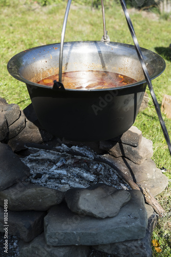 Pot goulash cooked over a fireplace on a tripod.
