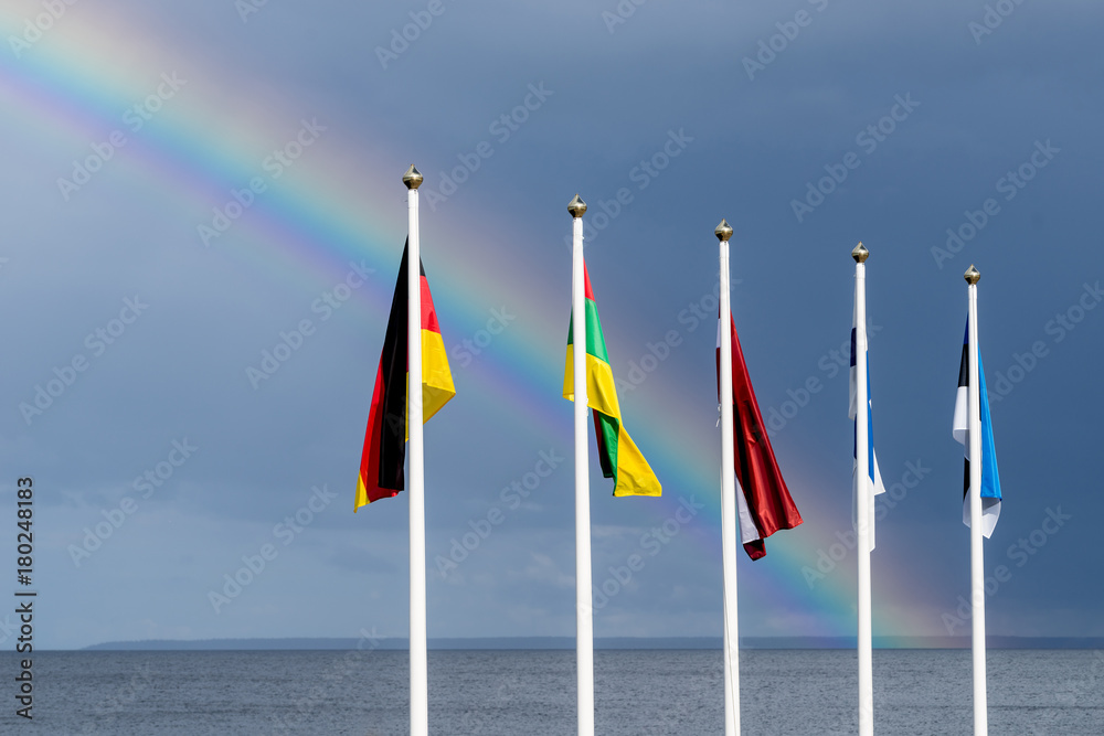 Estonian, Finnish, Lithuanian, Latvian and German flags waving in the wind, blue sky and rainbow in the background