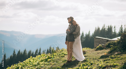 Newlyweds stand  smile and hug in mountains.