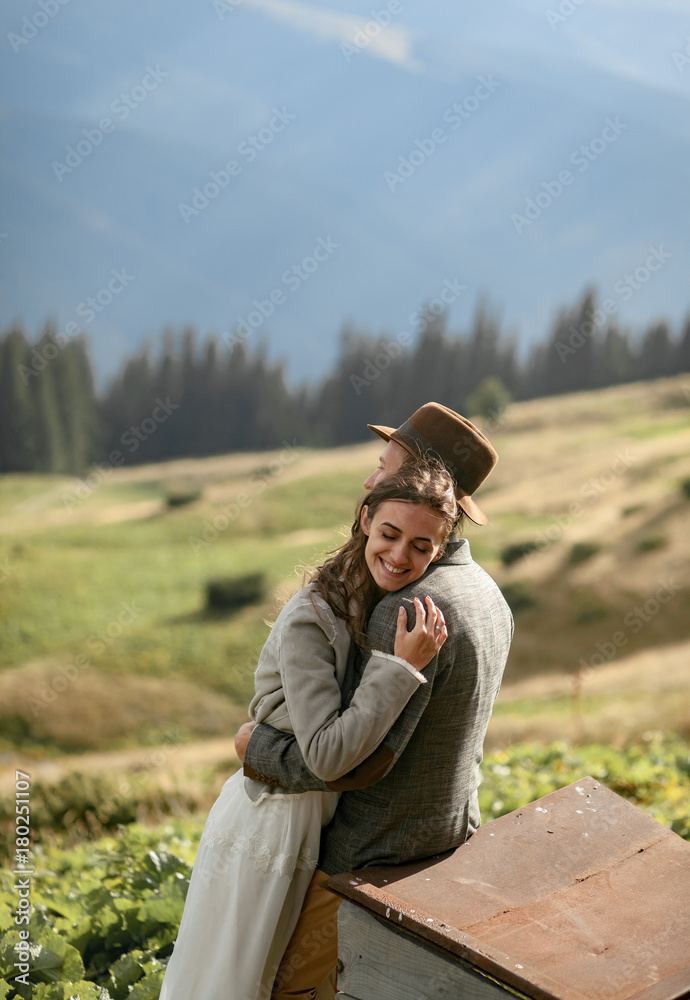 Newlyweds stand, smile and hug on background of mountains.