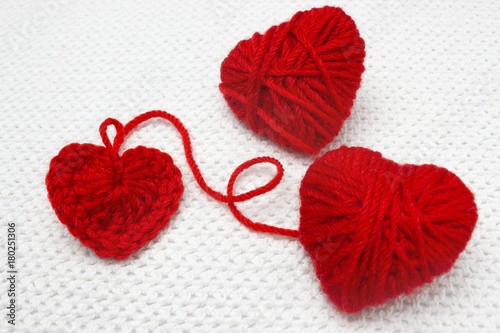 Red heart made of wool yarn and crochet heart. Soft focus. Handmade crocheted wool organic red heart. Old metal crocheting hook and two red yarn ball like a heart on the white crochet background.