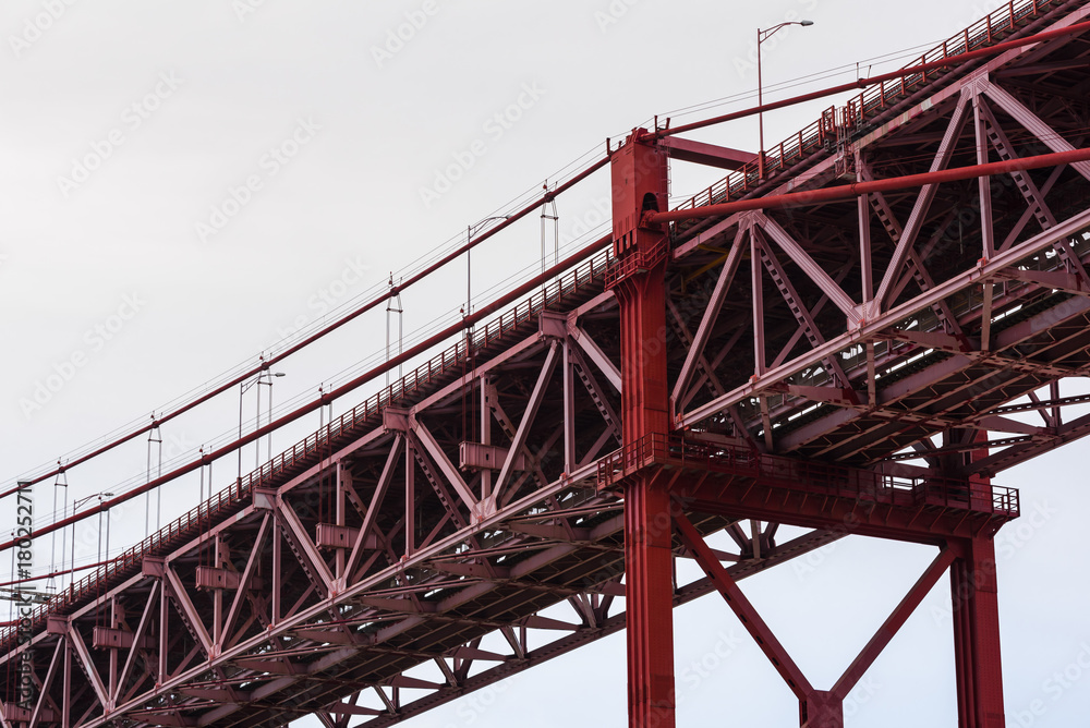 Close-up of red steel beam suspension bridge against grey sky